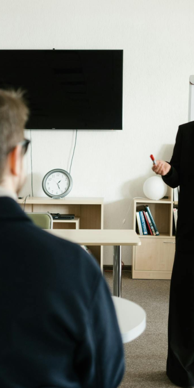 Businesswoman giving presentation in office with bookshelves and clock.